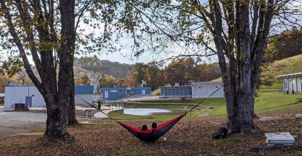 two people in a hammock overlooking a pond and telescopes